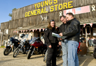 3 motorcycle riders with motorcycles looking at map in front of young's general store