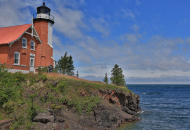 lighthouse with red brick building on the edge of a cliff surrounded by water